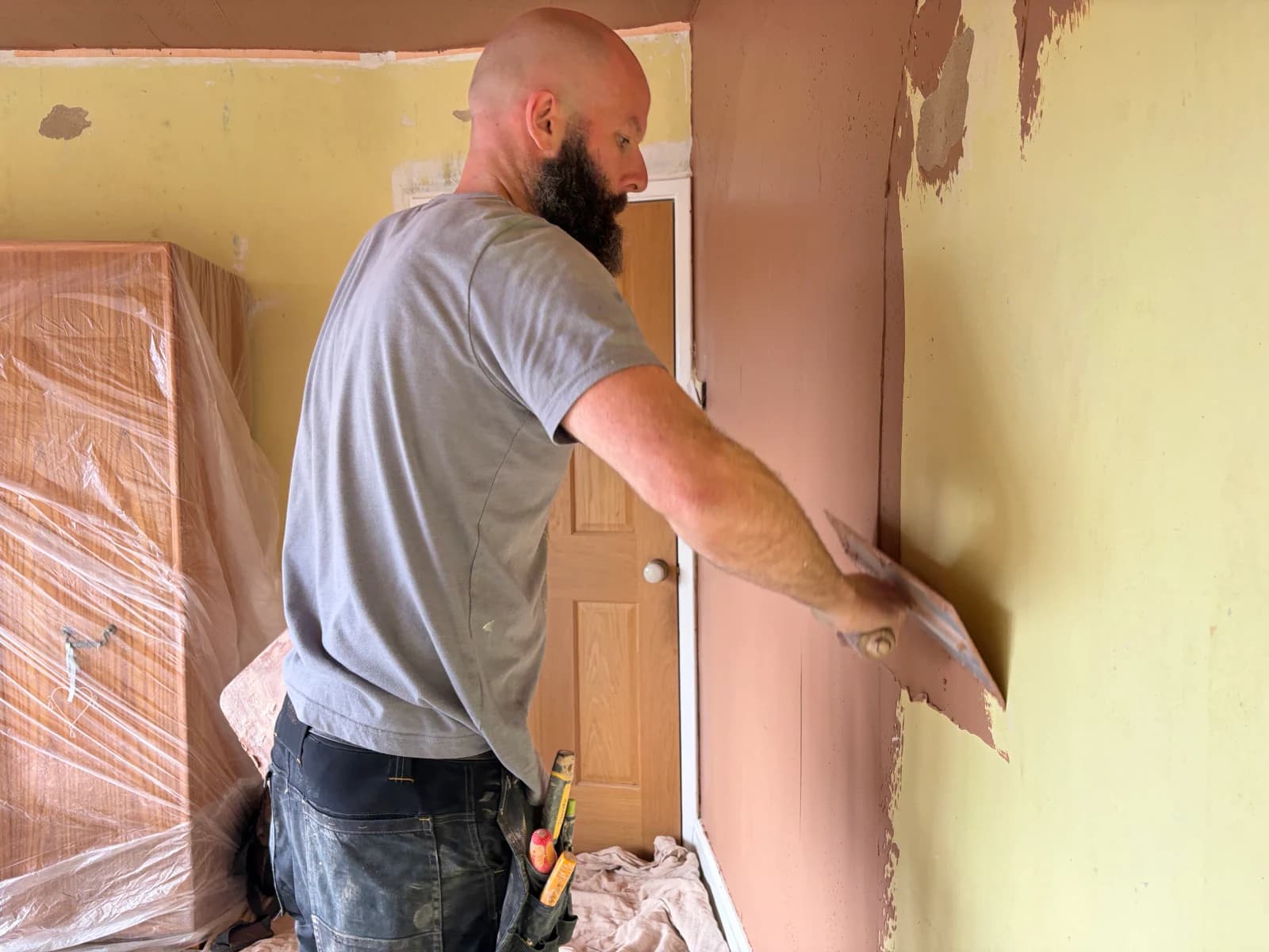 Plasterer applying a skim coat beside the protected wardrobe in the Allestree bedroom